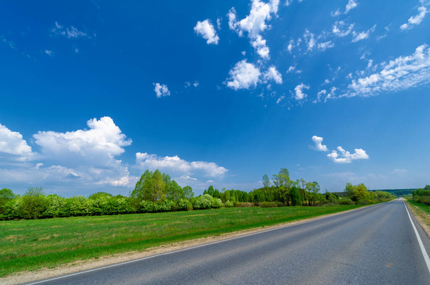 lente foto genomen met een groothoek lens, lokale snelweg, fel groene bomen, wolken in de blauwe lucht - Foto, afbeelding
