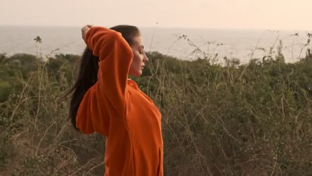Side view of Carefree pretty athletic woman in earphones preparing to run at seashore - Filmati, video