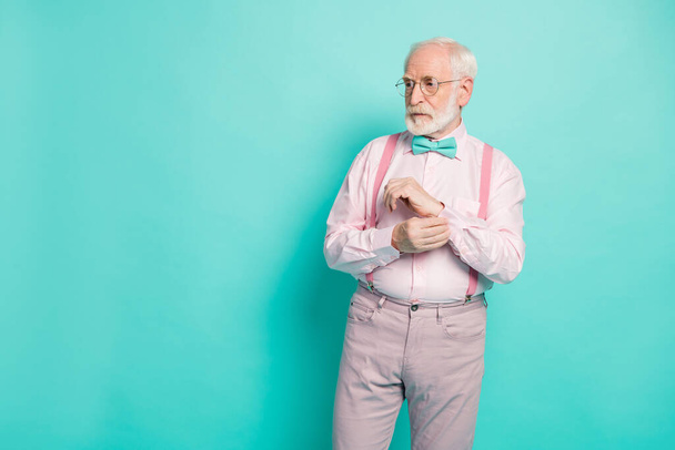 Photo of attractive serious hipster grandpa preparing senior meeting party buttoning sleeve look empty space wear specs pink shirt suspenders bow tie pants isolated teal color background - Fotoğraf, Görsel