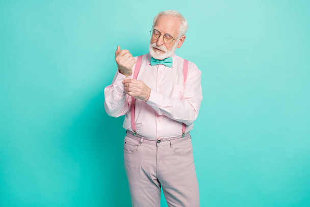 Photo of attractive hipster grandpa preparing senior meeting party buttoning sleeve carefully wear specs pink shirt suspenders bow tie pants isolated teal color background - Valokuva, kuva