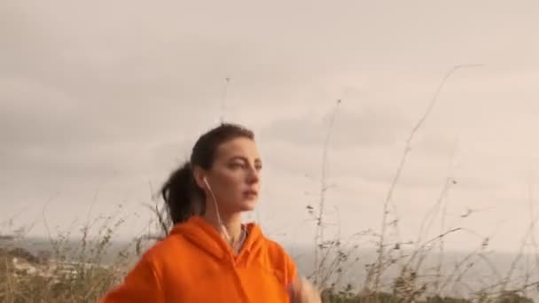 Serious pretty athletic woman in earphones running at seashore - Filmati, video