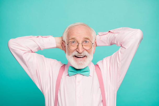 Closeup photo of funny grandpa positive facial expression good mood hands behind head look up empty space wear specs pink shirt suspenders bow tie isolated bright teal color background - Фото, зображення