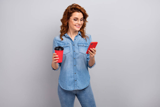 Portrait of positive cheerful woman rest relax after working day use smartphoen check social media news posts comments wear good look denim clothes isolated over grey color background - 写真・画像