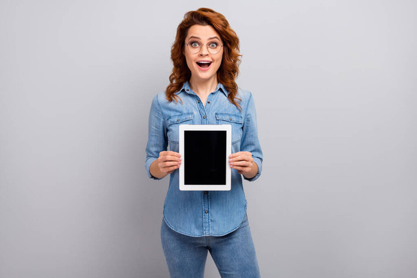 Portrait of astonished ginger hair woman hold tablet demonstrate incredible new modern technology ads promo impressed scream wow omg wear good look clothes isolated grey color background - 写真・画像