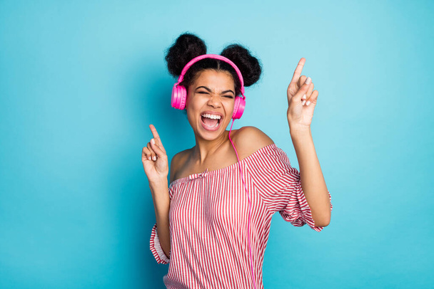 Photo of funny crazy dark skin lady listen music modern earphones sing favorite song raise fingers dancing wear trendy red white striped shirt off-shoulders isolated blue color background - Zdjęcie, obraz