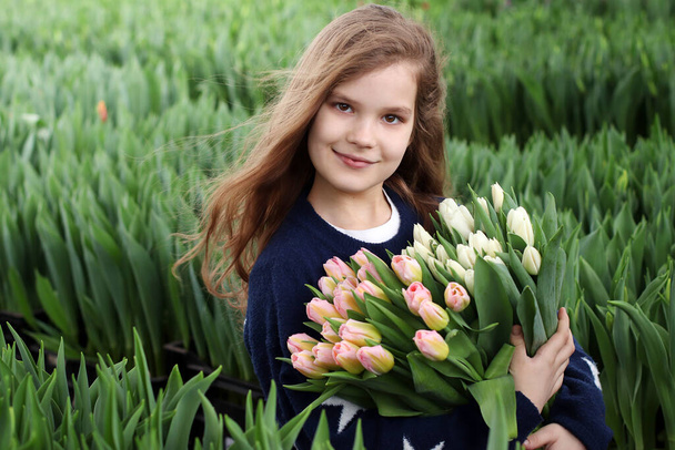 Девушка с букетом тюльпанов. Садовник-флорист держит букет цветов, стоя в теплице, где выращивают тюльпаны.
 - Фото, изображение