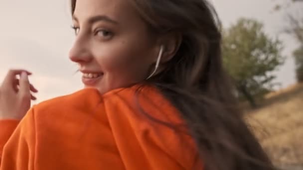 Vista posterior de la mujer atlética bonita juguetona en los auriculares que se divierten y caminar en la orilla del mar
 - Metraje, vídeo