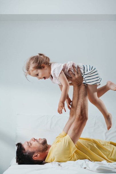 Father and daughter playing on bed - Фото, изображение