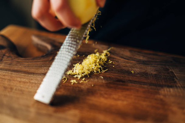 Female chef grating lemon zest on a wooden board - Foto, Imagen