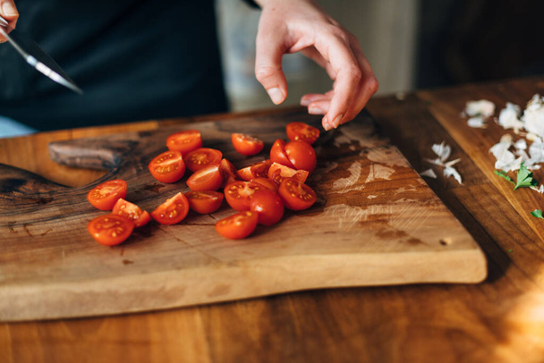 Chef chopping cherry tomatoes with knife on a wooden board - Fotó, kép