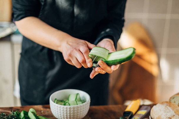 Female chef peeling skin of a cucumber - Foto, Imagem