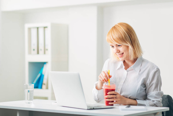 Attractive Woman Drinking Smoothie at the Office while reading Email and Laughing - Photo, Image