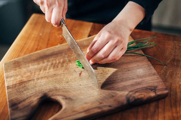 Female chef chopping spring onions on a wooden board - Foto, afbeelding