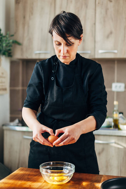Female chef cracking eggs into a glass bowl - 写真・画像