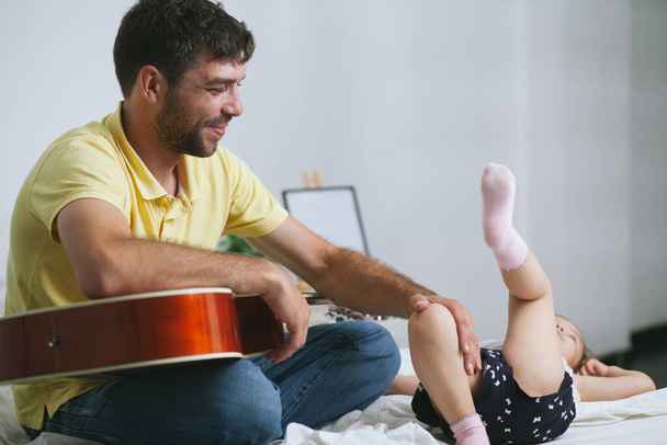 Young father having fun with his cute little daughter while teaching her how to play the guitar - Zdjęcie, obraz