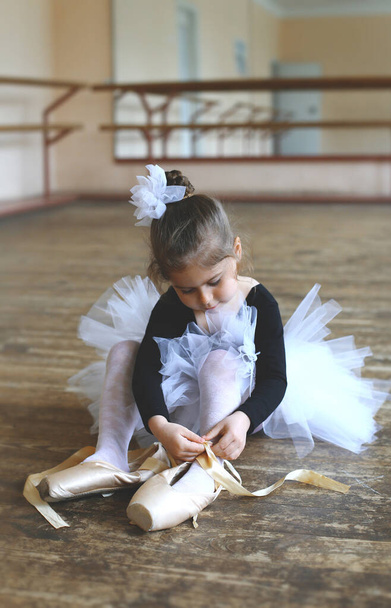 маленька балерина намагається зав'язати справжнє взуття, сидячи на підлозі в балетному класі
 - Фото, зображення