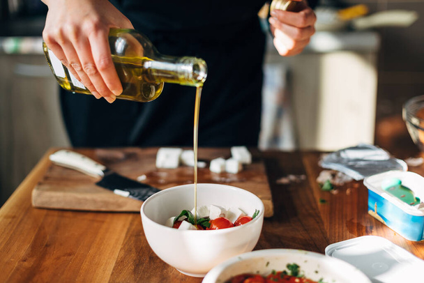 Female chef pouring olive oil on a greek salad - 写真・画像