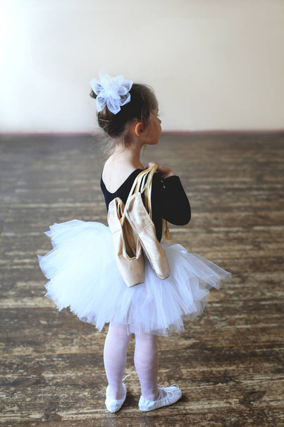 kleine ballerina staat met haar rug naar de camera met echte punten in haar hand - Foto, afbeelding
