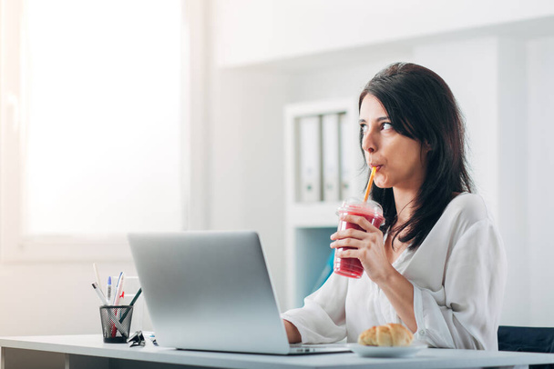 Attractive Woman Drinking Smoothie at the Office while reading Email - Photo, Image