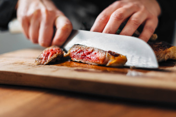 Chef slicing ribeye steak on a wooden board - Фото, зображення