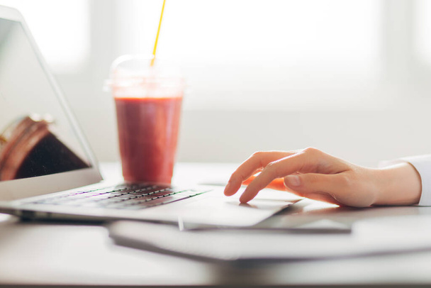 Detail of Woman's Hands typing on laptop with smoothie in office background - Valokuva, kuva