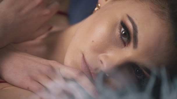 Blur effect portrait closeup woman lying touch face hand makeup eyes fluffy long eyelashes iris pure skin passion sensual lips romantic female brunette hair style date cosmetic beauty product feather. - Footage, Video