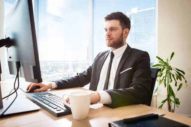 Молодий бізнесмен в офісі сидить за своїм столом
 - Фото, зображення