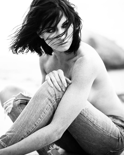 Hermosa dama en traje de baño negro se sienta en una playa de arena
 - Foto, imagen