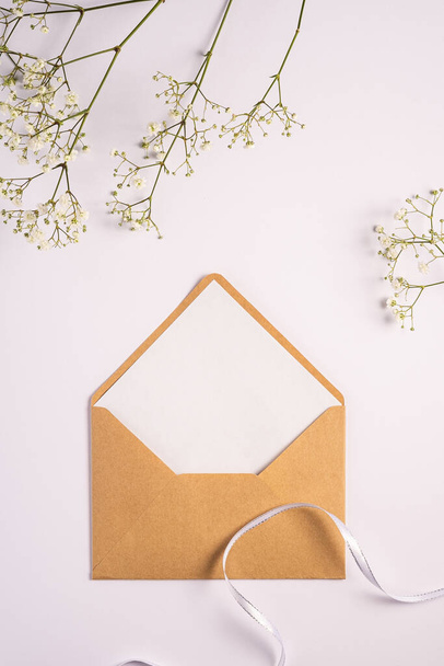 Крафт коричневый бумажный конверт с белой пустой картой, цветы гипсофилы и тканевая лента, белый фон, макет пустой буквы
 - Фото, изображение