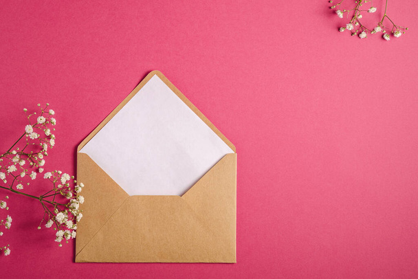 Kraftpapier bruine enveloppe met witte lege kaart, gypsophila bloemen, rood roze achtergrond, model template - Foto, afbeelding