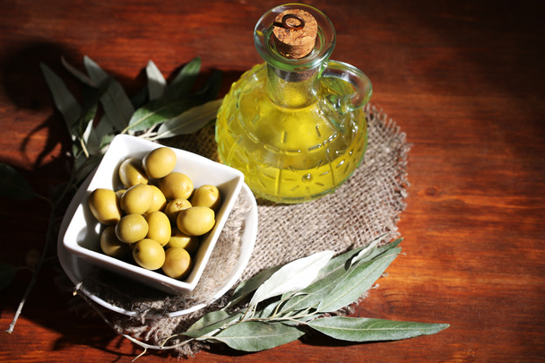 Olive oil and olives in bowl on sackcloth on wooden table - Фото, зображення