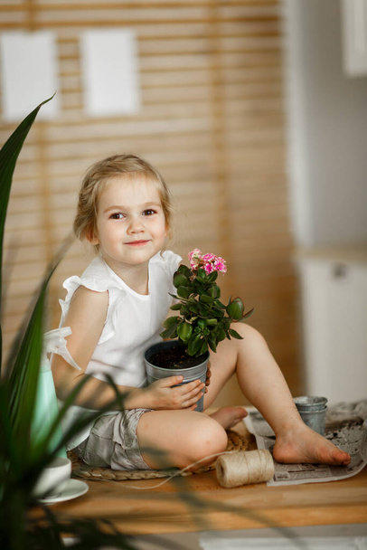 little girl with indoor flowers into pot - Fotó, kép