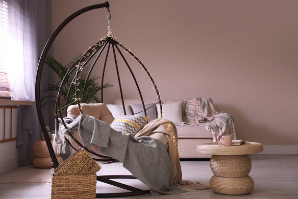 Cozy hanging chair with fairy lights in modern living room. Interior design - Φωτογραφία, εικόνα