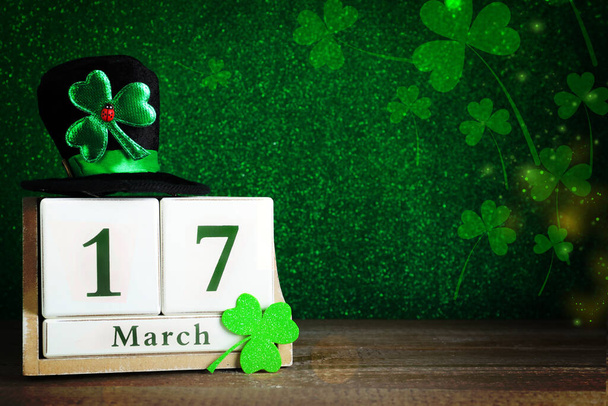 Black leprechaun hat, clover leaf and wooden block calendar on table, space for text. St. Patrick's Day celebration - Фото, зображення
