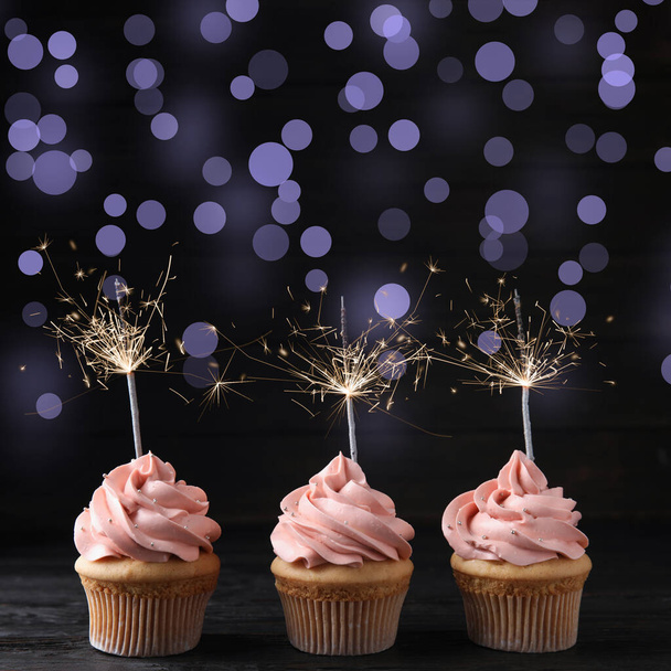 Cupcakes de cumpleaños con bengalas sobre mesa de madera sobre fondo oscuro
 - Foto, imagen