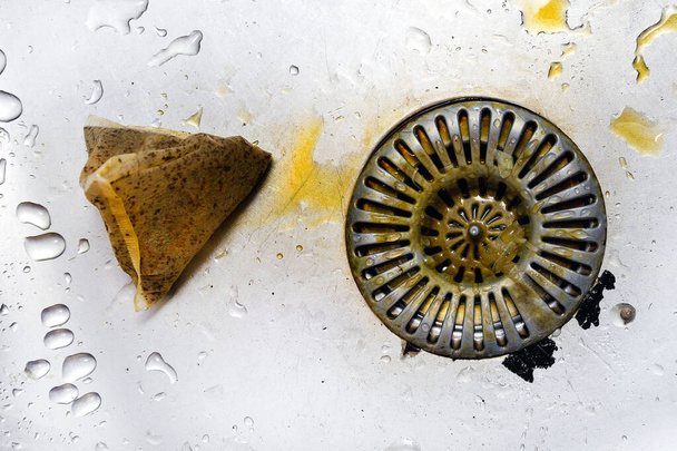 Coador sujo em pia de aço inoxidável, lodo e resíduos sujos, má higiene da cozinha. Saco de chá usado jogado na pia
. - Foto, Imagem