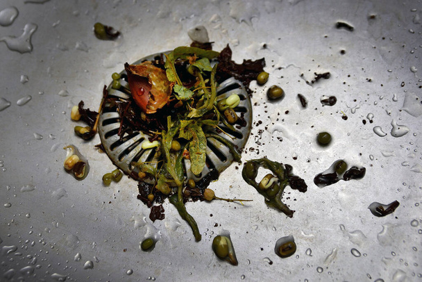 Colador obstruido desagradable en fregadero inoxidable, verduras húmedas podridas en los residuos, mala higiene de la cocina
. - Foto, Imagen