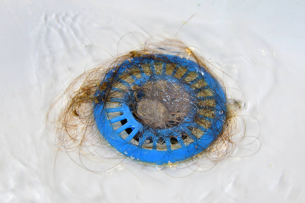 Cheveux tombés dans une passoire bleue dans l'évier, mauvaise hygiène, écoulement d'eau bouché
. - Photo, image