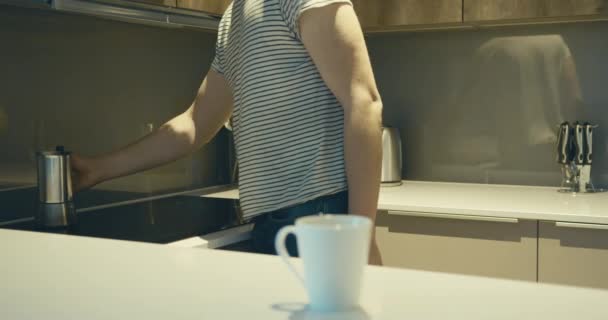 A young man is placing his coffee pot on the induction cooker in his kitchen - Imágenes, Vídeo