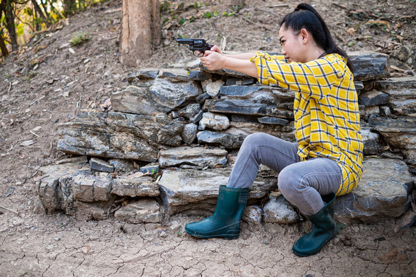 Retrato de la granjera asea mujer con una bota en el disparo de arma de fuego de edad en la granja, Niña sentada en la actitud de apuntar y mirar a través de la pistola de visión
 - Foto, Imagen