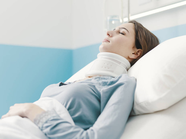 Young woman lying in a hospital bed with IV drip and a cervical collar, she is hospitalized after a serious accident - Foto, afbeelding