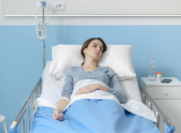 Young female patient lying in bed with IV drip, medicine and treatment concept - Foto, afbeelding