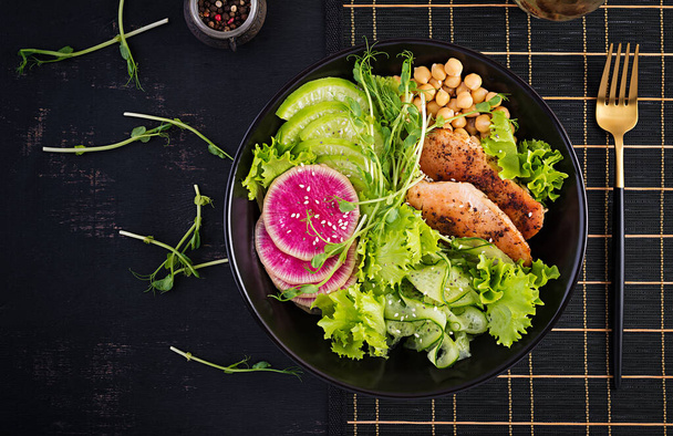 Trendy salad. Buddha bowl dish with chicken fillet, chickpea, cucumber, radish,  fresh lettuce salad, pea sprouts  and chia seeds. Healthy food. Top view, overhead, copy space - Фото, изображение