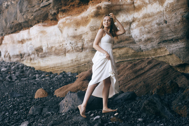 Чудова дівчина в довгій білій сукні на березі океану. Довгошерста дівчина успадкована природою, горами, камінням, пляжем. Дівчина у відпустці, легка сукня, літо, побачення. Наречена
 - Фото, зображення