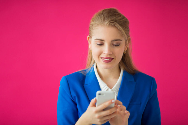 beautiful young woman in a blue jacket on a pink background with a phone in her hand - 写真・画像