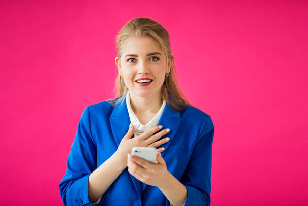  beautiful young woman in a blue jacket on a pink background with a phone in her hand - 写真・画像