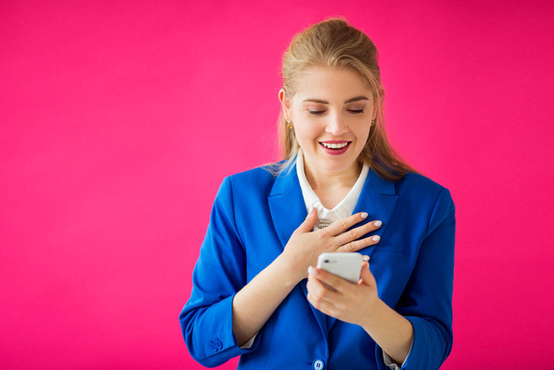  携帯電話を手にピンクの背景に青いジャケットを着た美しい若い女性が - 写真・画像