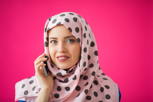 beautiful young woman in a scarf on a pink background with a phone in her hand - Foto, imagen