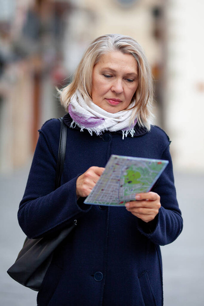Mulher madura turista com um mapa na mão caminha pelas ruas da cidade
 - Foto, Imagem