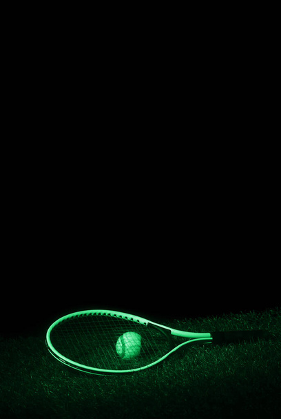 Tennis racket with tennis balls on grass with black background and copy space. Green filter - Photo, Image